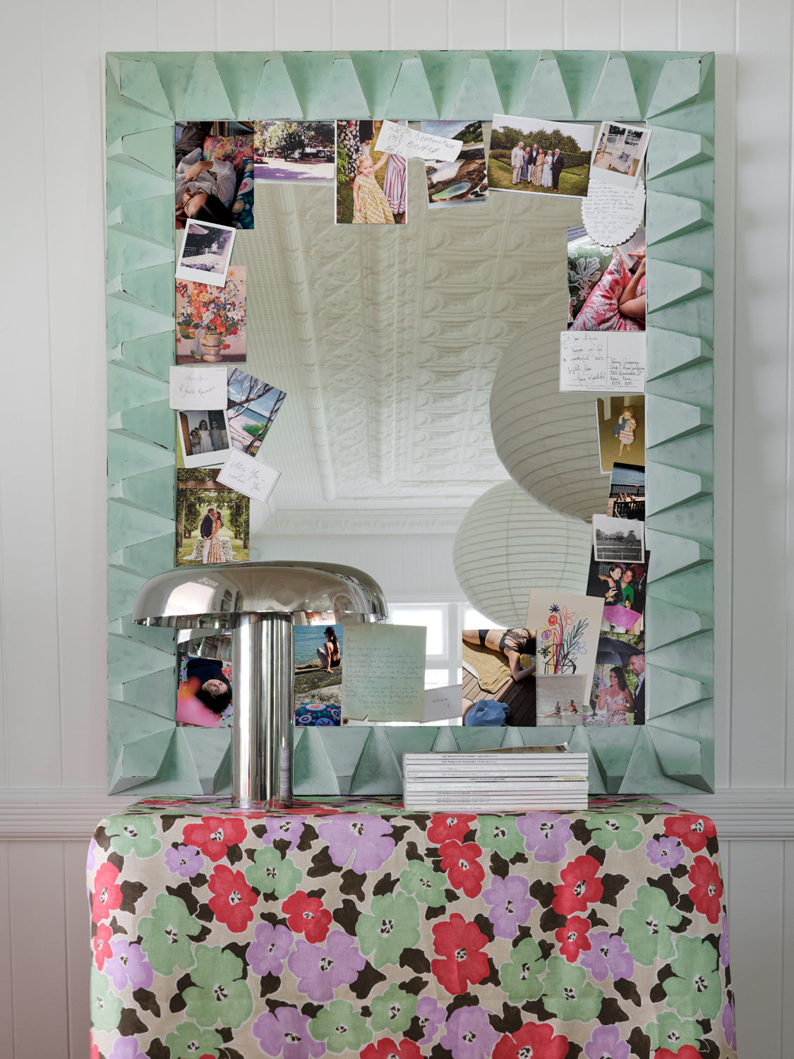 A mirror cluttered with photos and notes rests on a table draped in painterly floral fabric yardage.