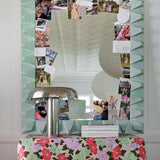 A mirror cluttered with photos and notes rests on a table draped in painterly floral fabric yardage.