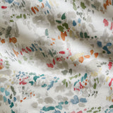 Draped fabric yardage in a painterly cloud print in shades of red, green, tan and blue on a cream field.