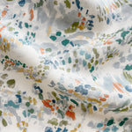 Draped fabric yardage in a painterly cloud print in shades of red, green, yellow and blue on a cream field.