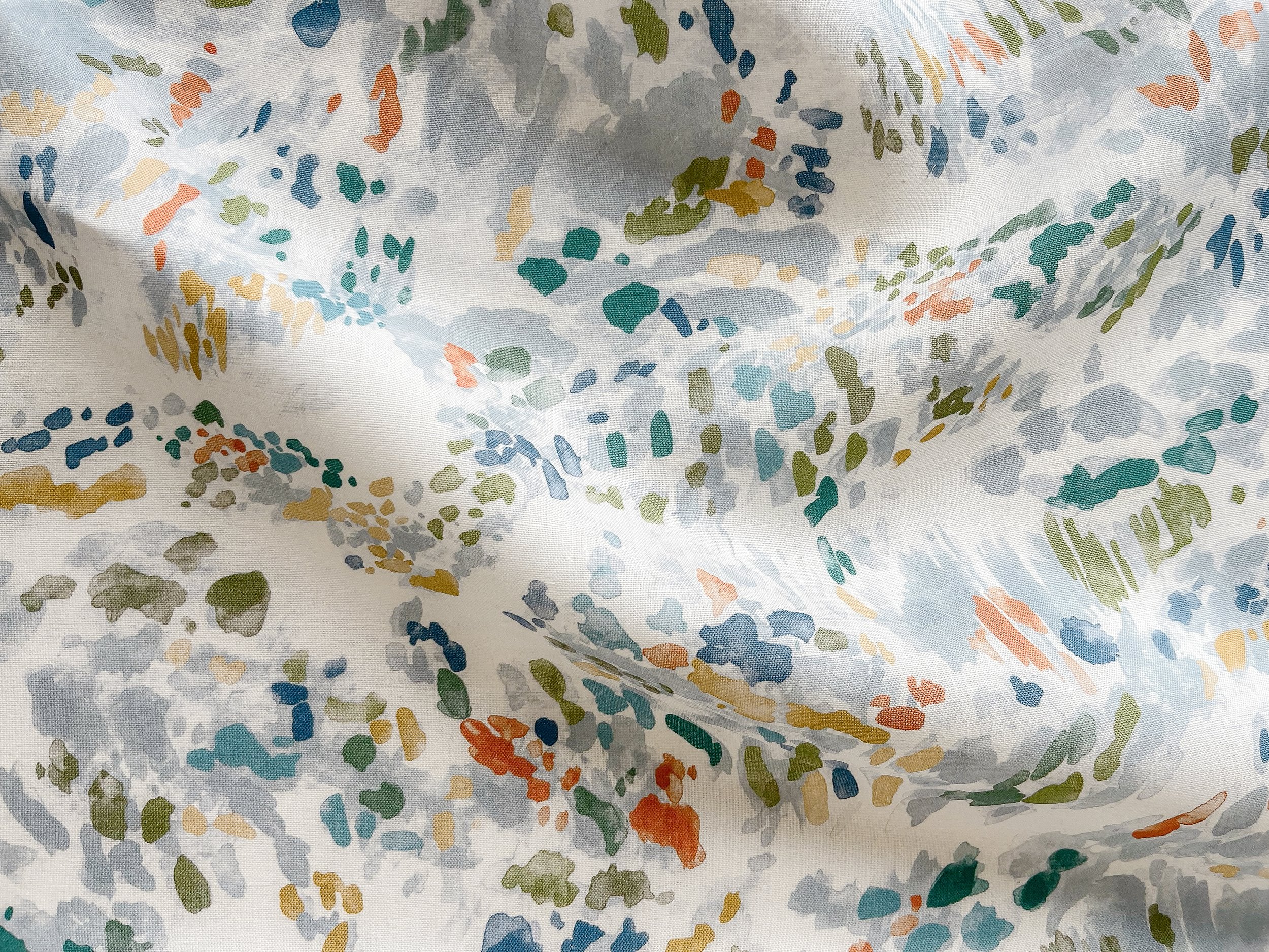 Draped fabric yardage in a painterly cloud print in shades of red, green, yellow and blue on a cream field.