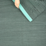 A woman's hand folding a woven leather rug in a herringbone pattern in dark green with turquoise accents.