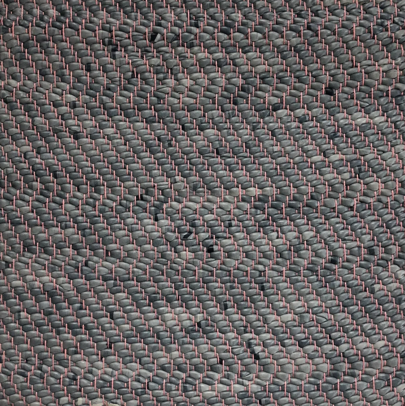 Detail of a woven leather rug in a herringbone pattern in mottled gray with pink accents.