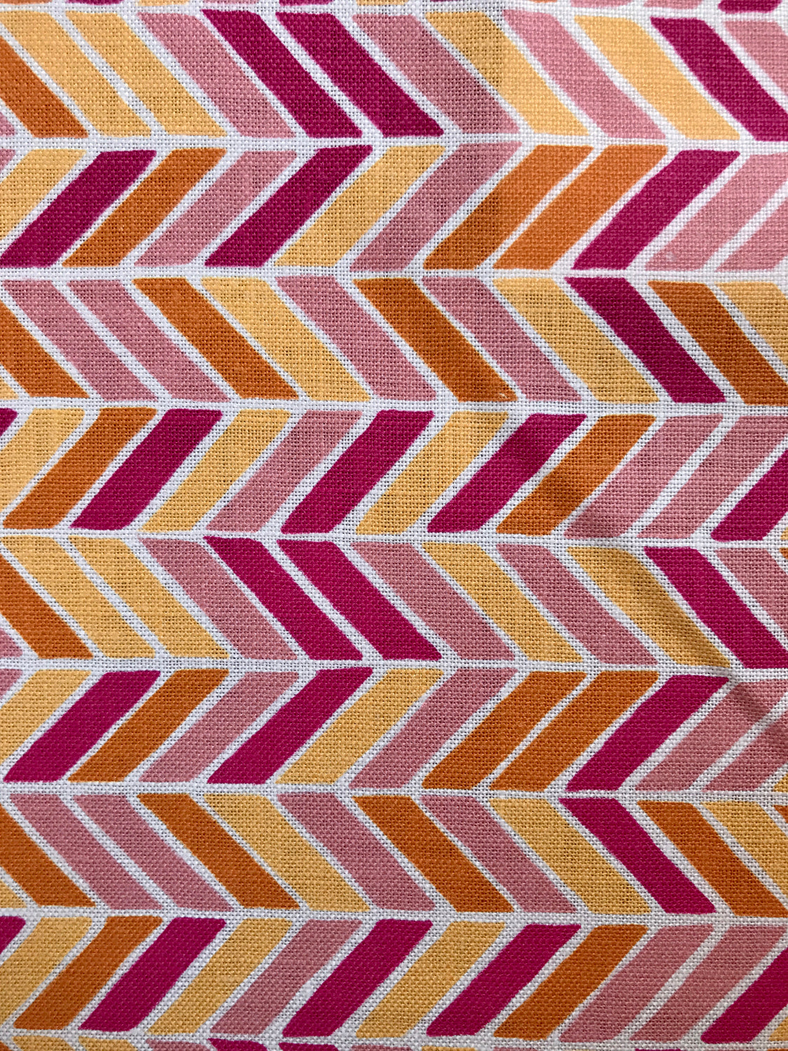 Detail of fabric in a geometric herringbone print in pink, orange and yellow on a white field.