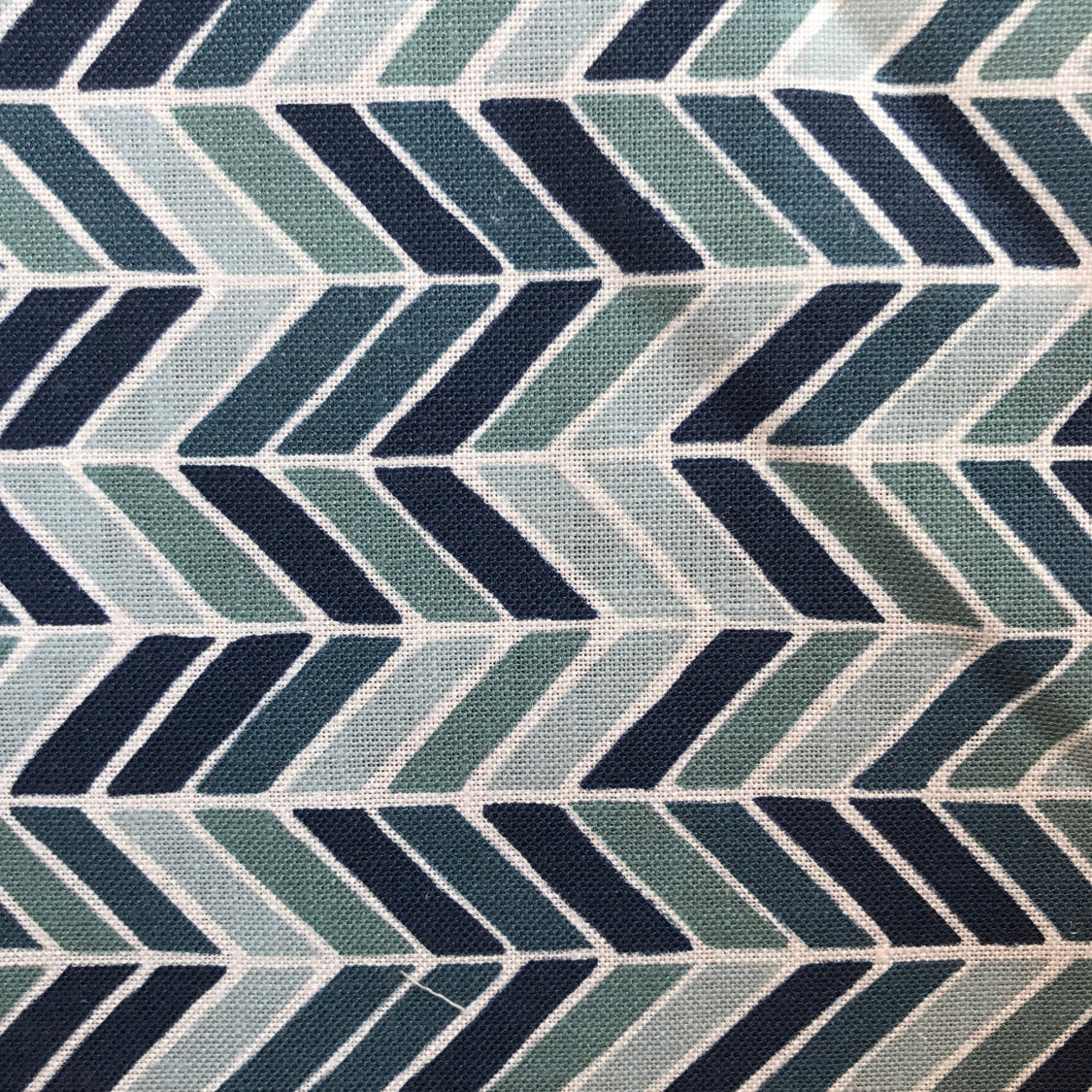 Detail of fabric in a geometric herringbone print in blue, turquoise and navy on a white field.