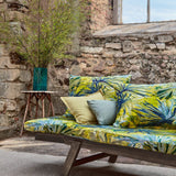 An outdoor space with a sofa upholstered in a painterly palm tree print in shades of yellow, blue and green.