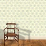 A wooden chair stands in front of a wall papered in a playful floral stripe in blue-gray on a light blue field.