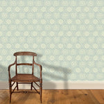 A wooden chair stands in front of a wall papered in a playful floral stripe in cream on a blue-gray field.