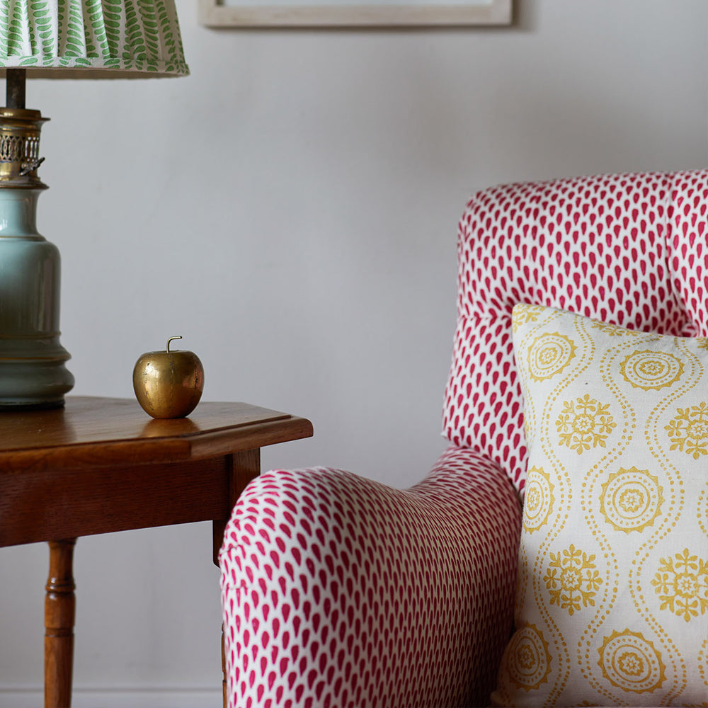 An armchair upholstered in a red and white dot print, topped with a floral throw pillow in yellow and cream.