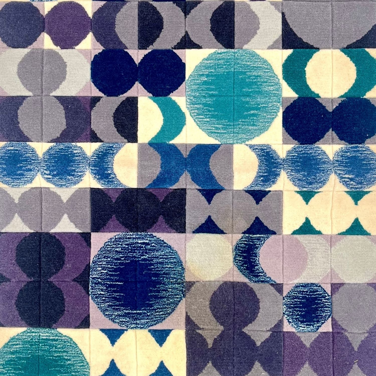 Detail of rug with a geometric and circular pattern in shades of blue, purple, and ivory.