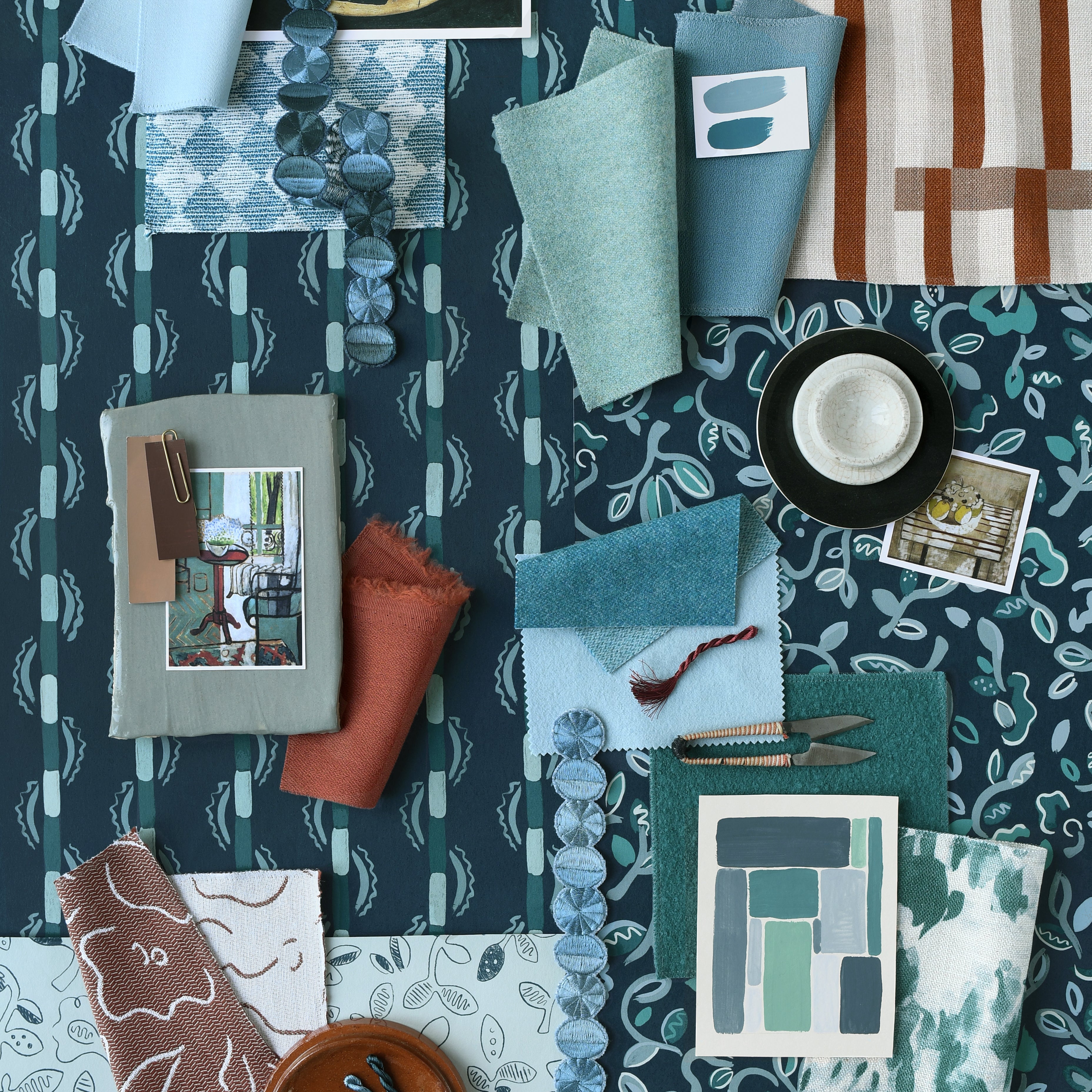 Collection of fabric swatches and samples arranged on a patterned surface in shades of teal, blue and rust. 