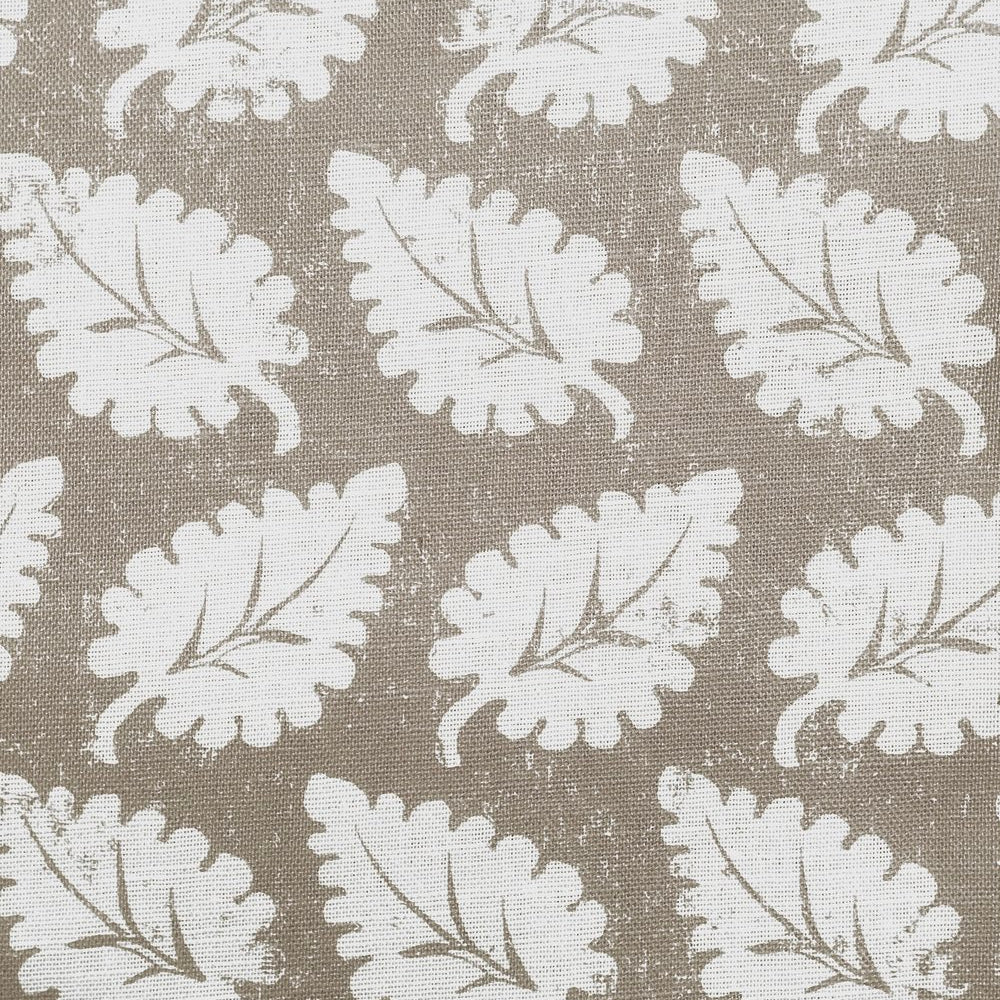 Detail of fabric in a repeating leaf print in white on a tan field.