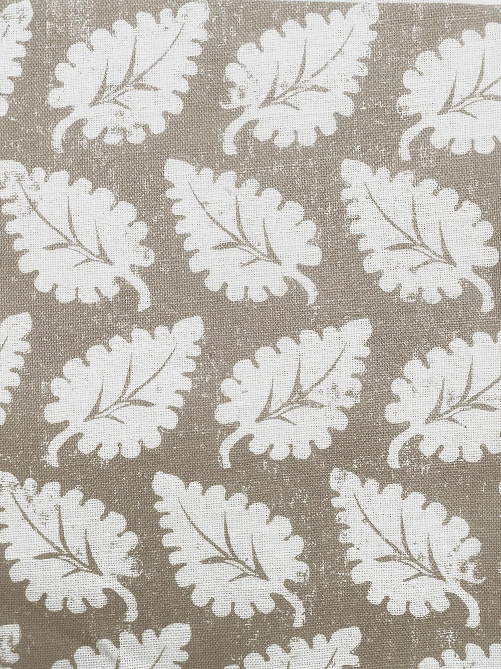 Detail of fabric in a repeating leaf print in white on a tan field.