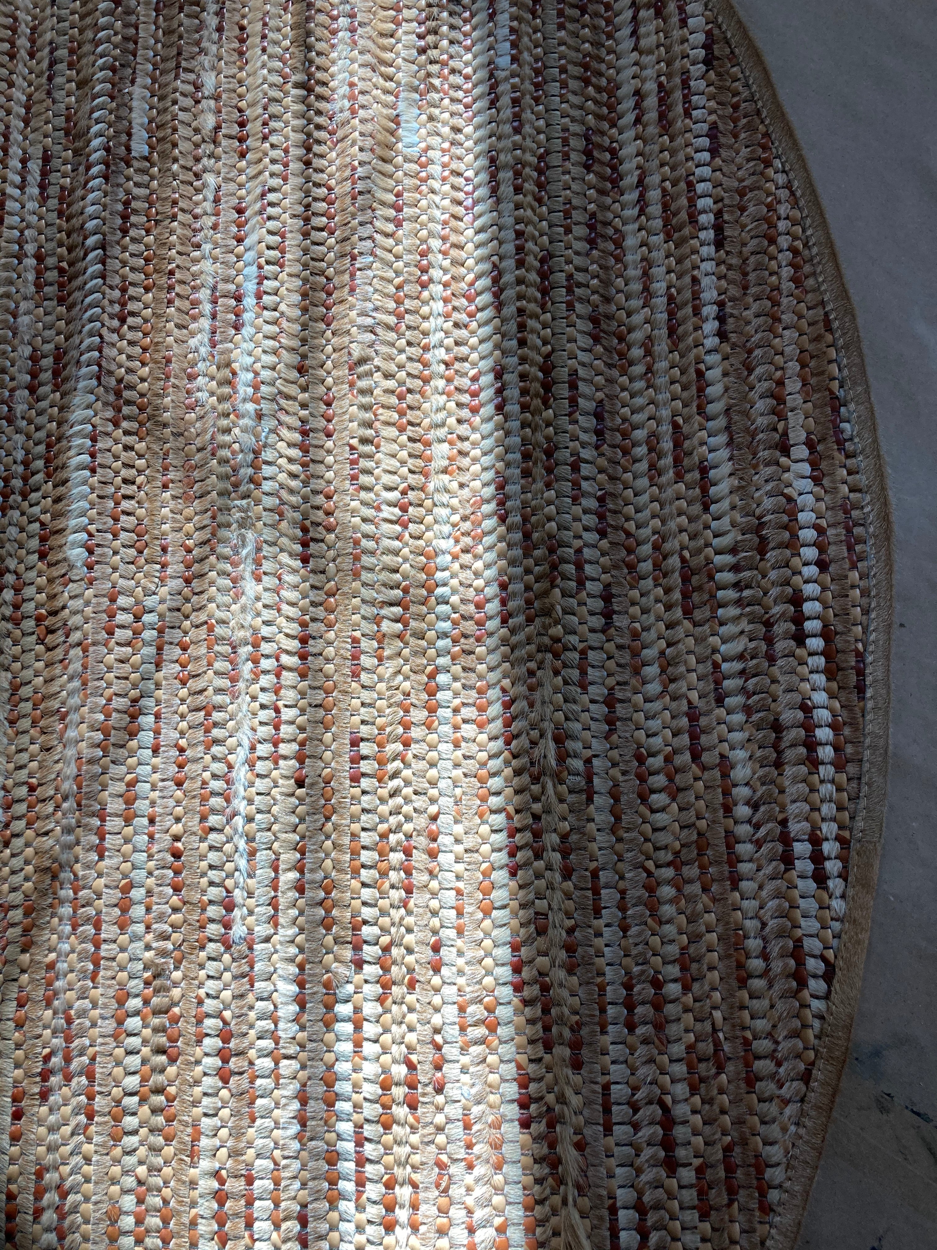 Overhead shot of a woven leather rug in a stripe dgrid texture in shades of brown and cream.