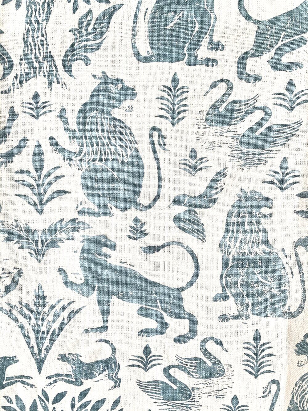 Close-up of fabric in a lion and plant print in blue-gray on a mottled white field.