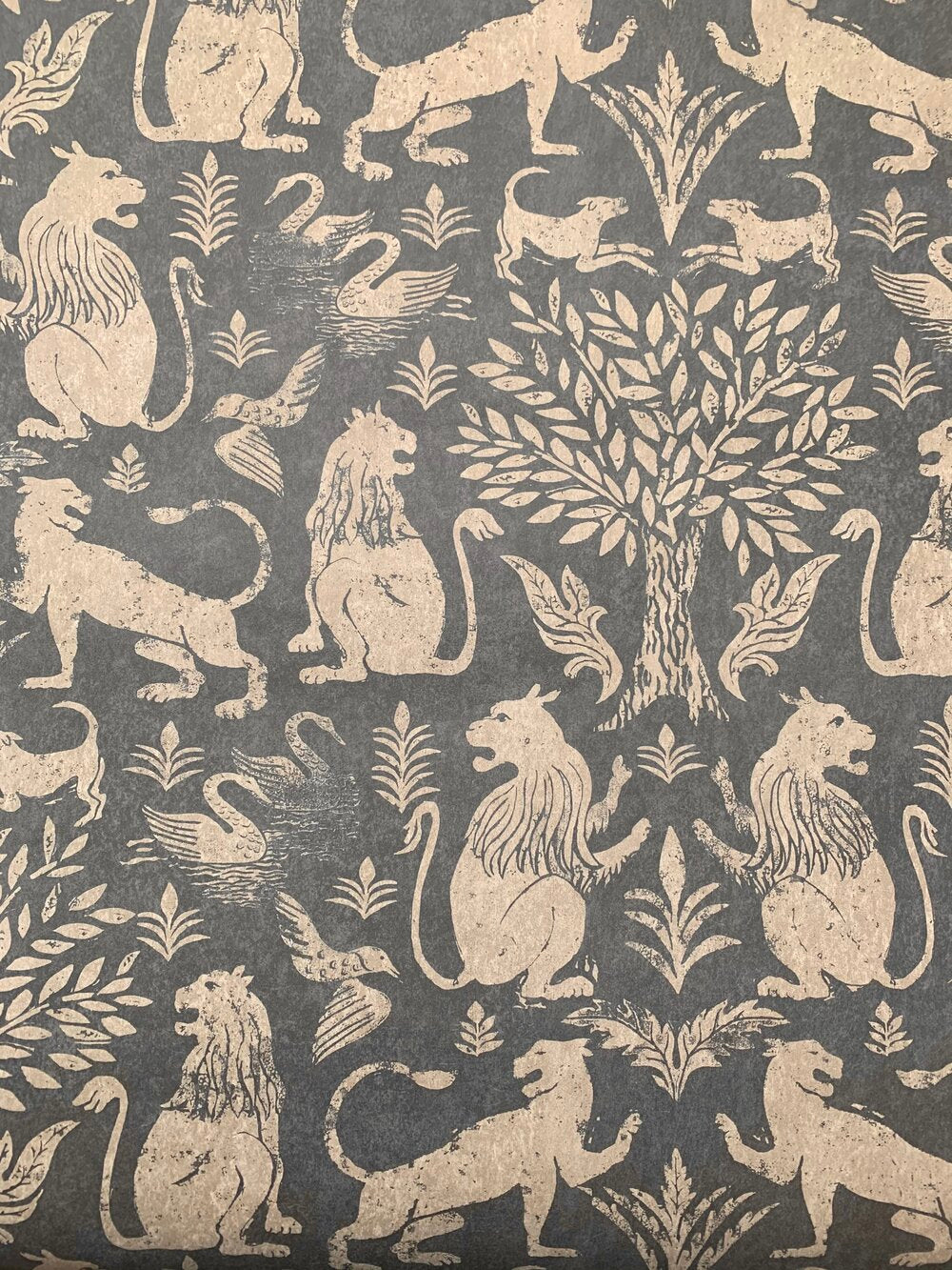 Detail of wallpaper in a lion and plant print in cream on a mottled gray field.