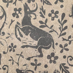 Close-up of wallpaper in a deer, leaf and flower print in gray on a mottled tan field.