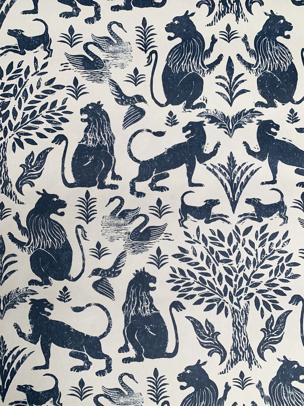 Detail of wallpaper in a lion and plant print in navy on a mottled cream field.