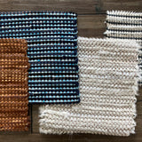 A row of woven leather rug swatches, all with striped grid textures, all in different colorways.