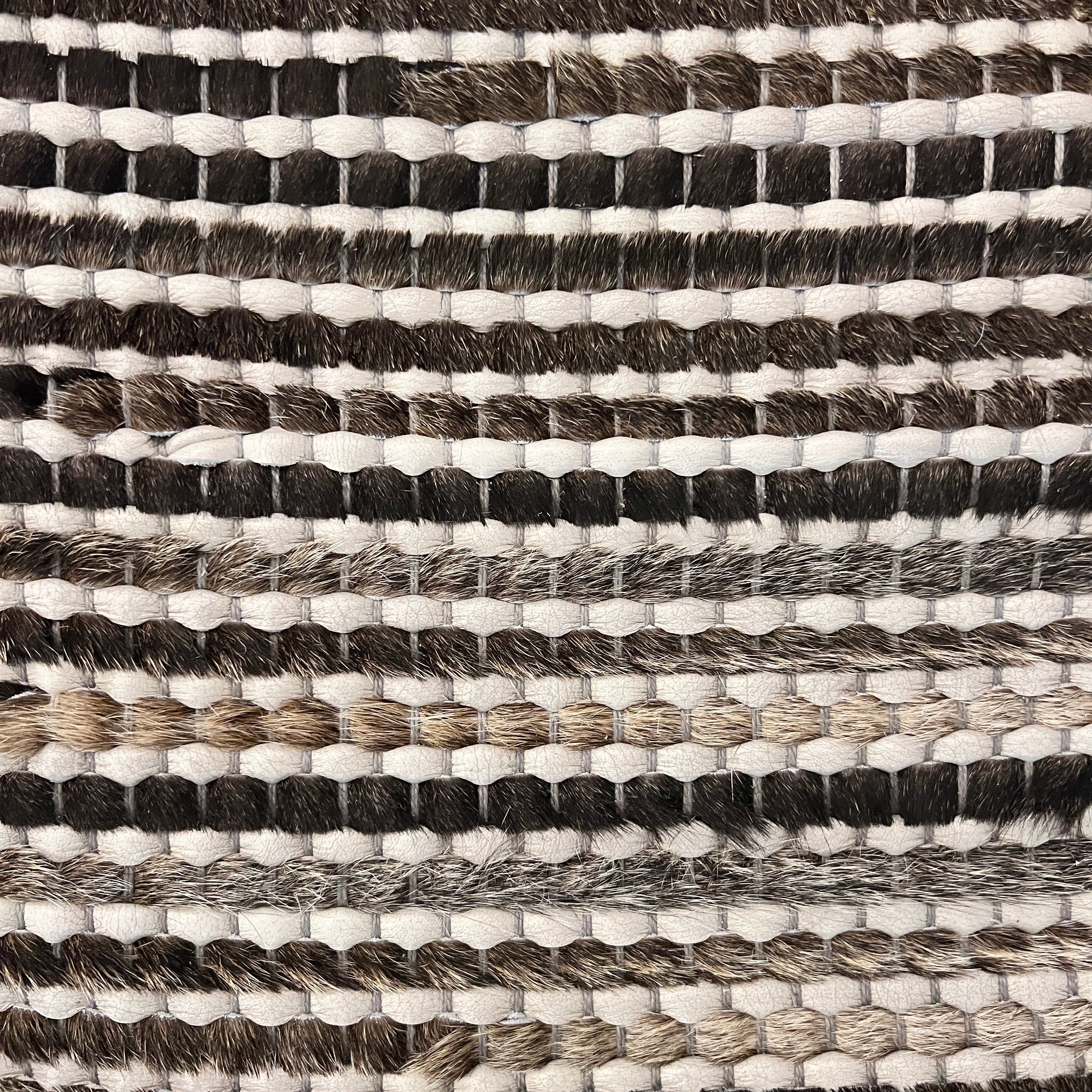 Detail of a woven leather rug in a striped grid texture in shades of brown and cream.