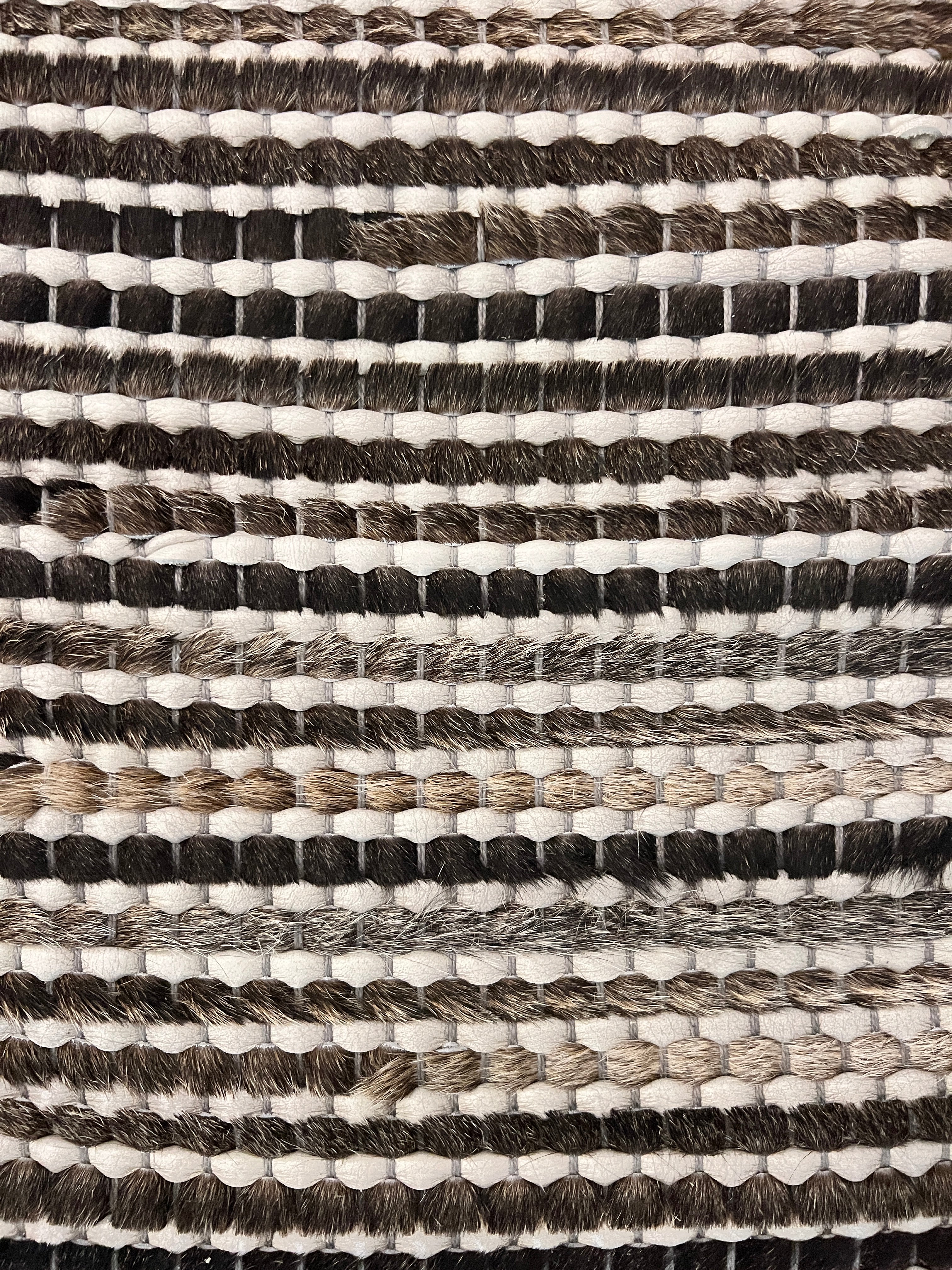 Detail of a woven leather rug in a striped grid texture in shades of brown and cream.