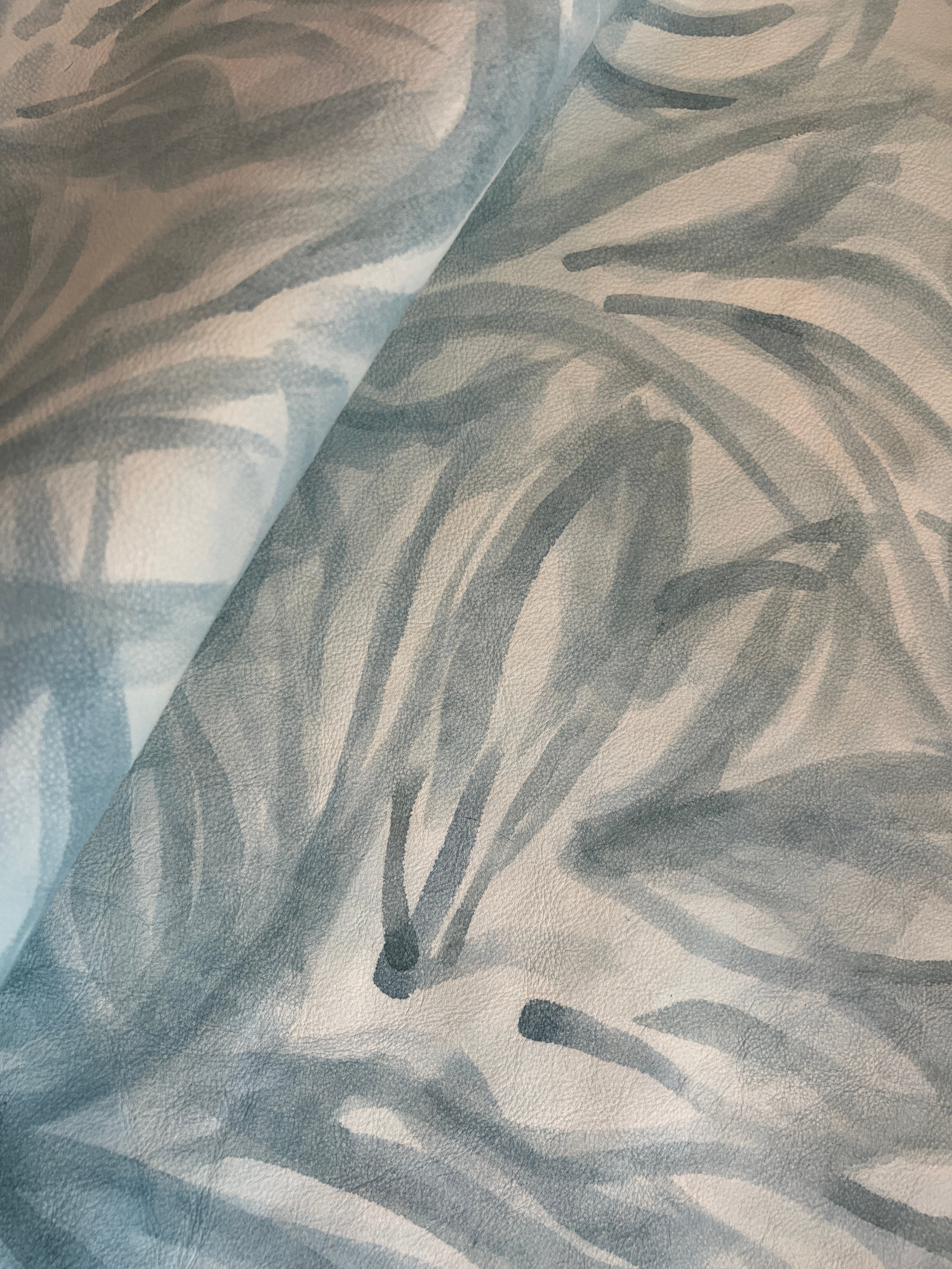 Draped upholstery leather in cream with a painterly botanical overlay in blue and gray.