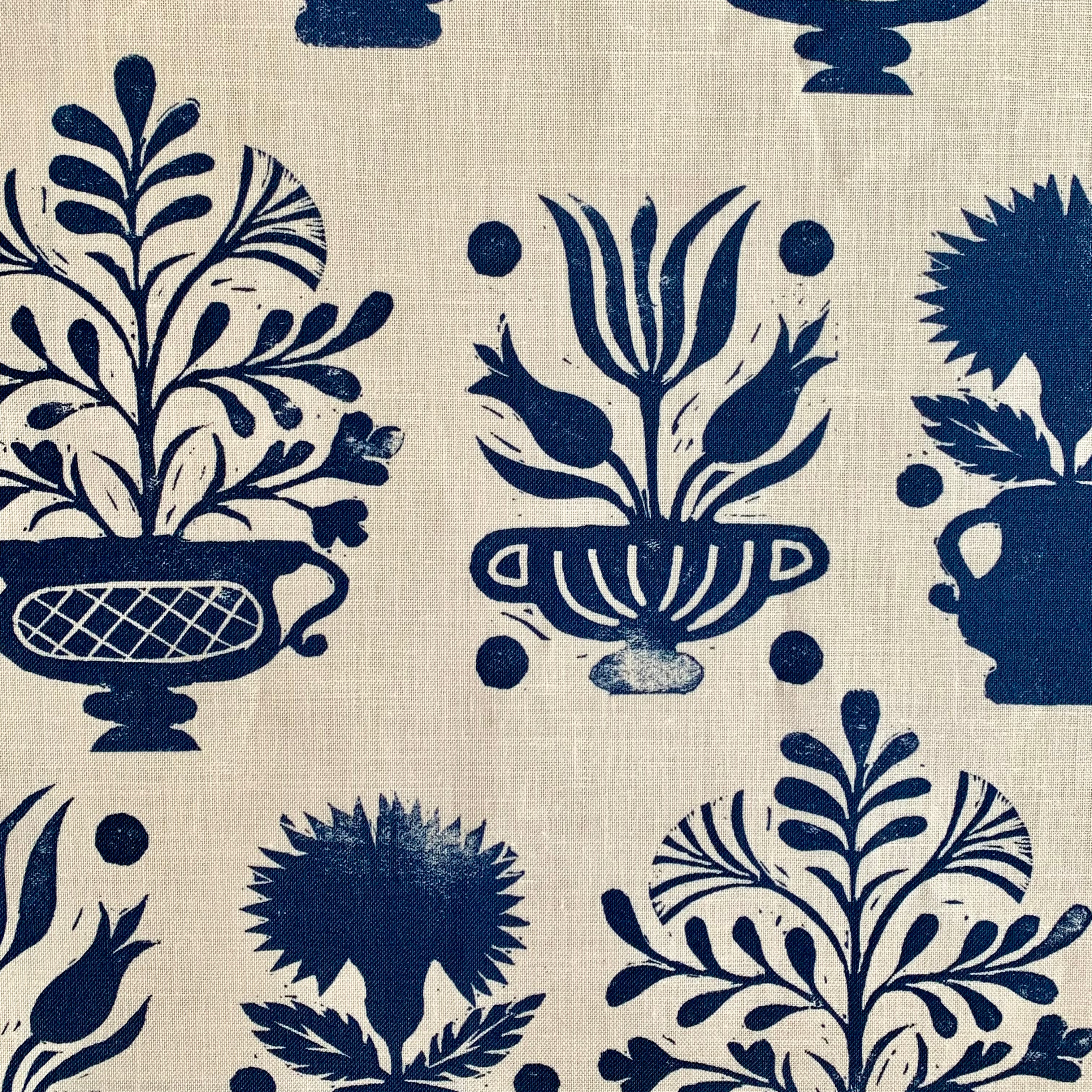 Close-up of fabric in a repeating vase and plant print in navy on a cream field.