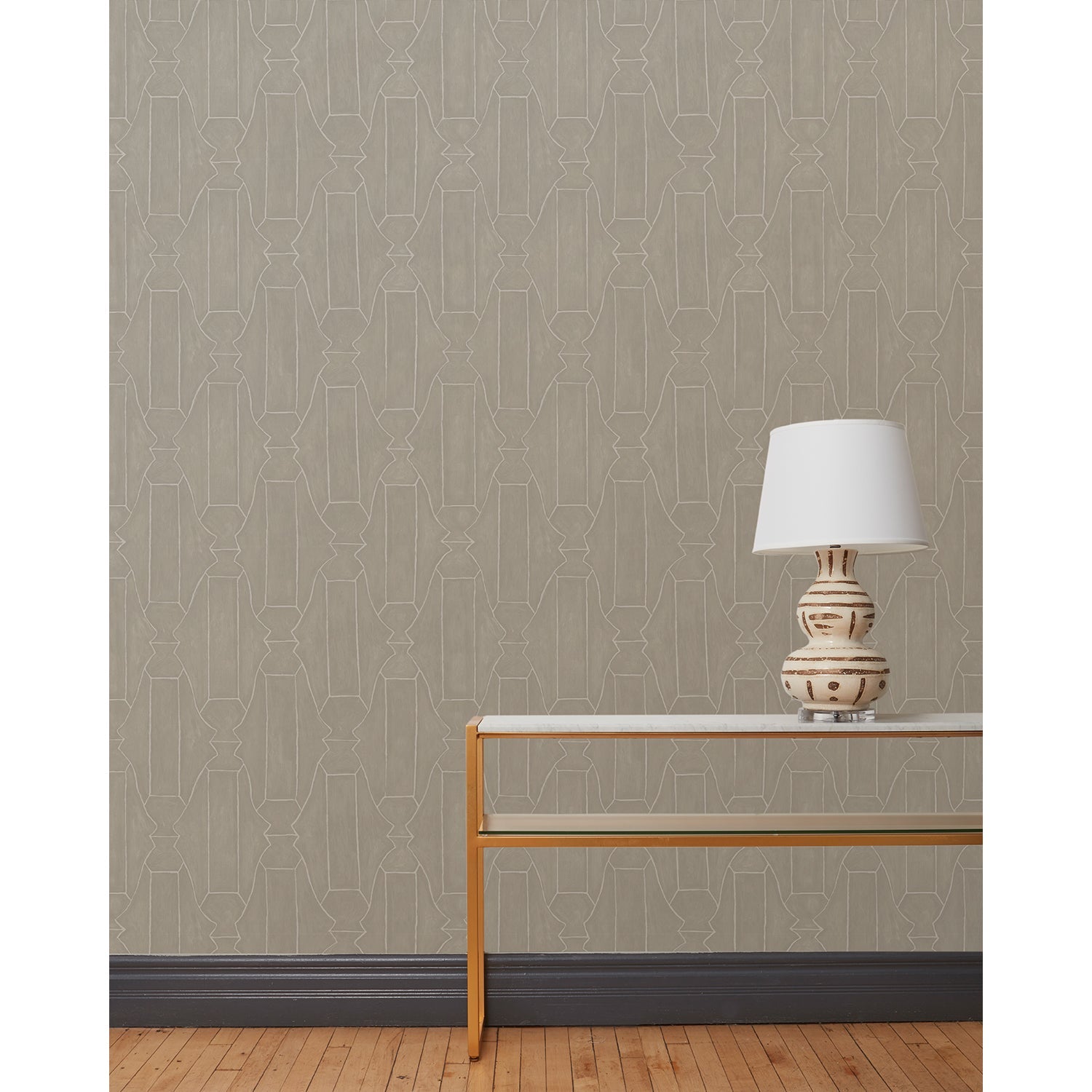 End table and white lamp in front of a wall papered in a repeating curvolinear print in white on a painted gray field.