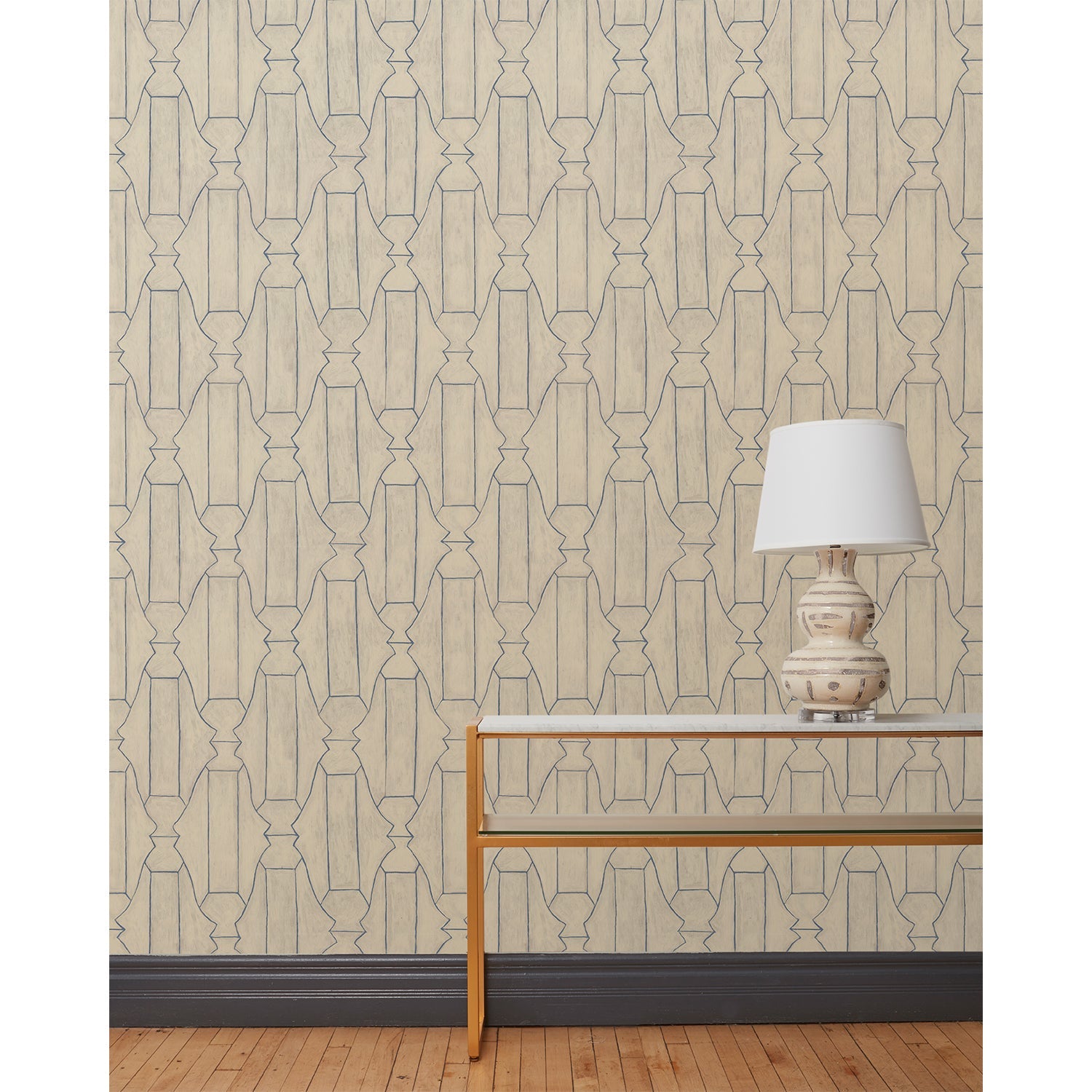 End table and white lamp in front of a wall papered in a repeating curvolinear print in navy on a painted tan field.
