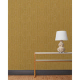 End table and white lamp in front of a wall papered in a repeating curvolinear print in cream on a painted gold field.