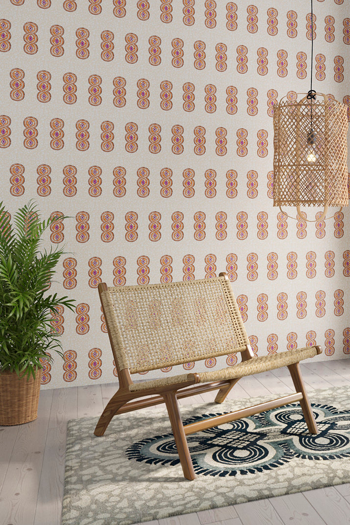 Styled living room tableau with a wall papered in an intricate curvilinear print in cream, orange and pink.