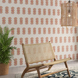 Styled living room tableau with a wall papered in an intricate curvilinear print in cream, orange and pink.