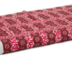 Partially unrolled fabric in an intricate curvilinear print in shades of red, orange and pink.