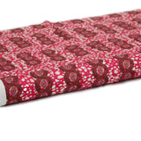 Partially unrolled fabric in an intricate curvilinear print in shades of red, orange and pink.