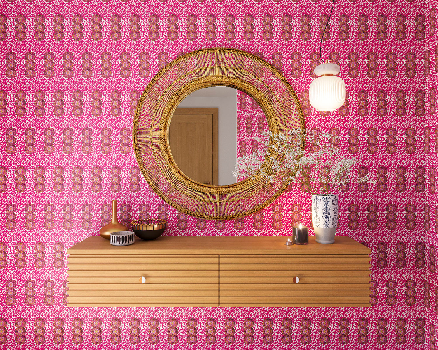 A floating shelf and statement mirror hang on a wall papered in a curvilinear print in pink, red, orange and white.
