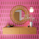 A floating shelf and statement mirror hang on a wall papered in a curvilinear print in pink, red, orange and white.
