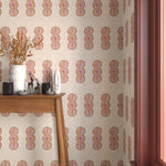 Interior with orange, pink and beige geometric wallpaper and matching trim with a wooden console table with white ceramic vases and mini ceramic sculptures. 