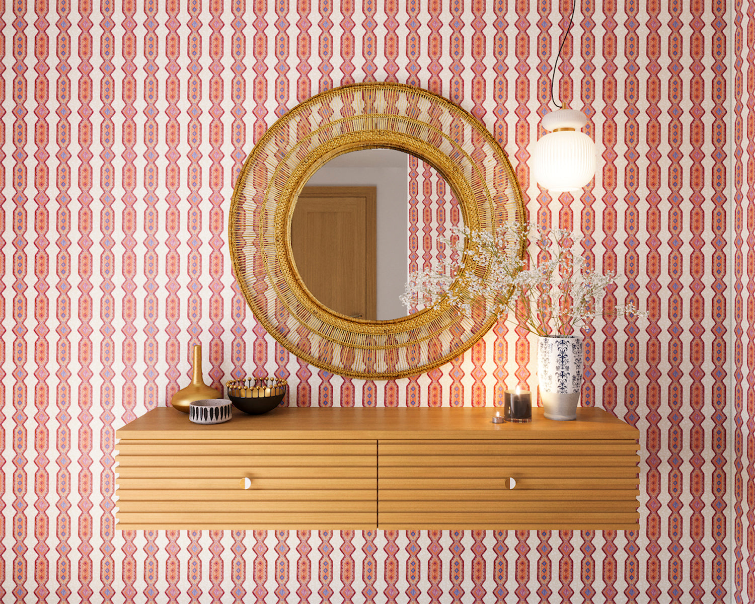 A floating shelf and statement mirror hang on a wall papered in a geometric stripe pattern in orange, blue, red and cream.