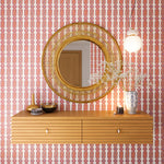 A floating shelf and statement mirror hang on a wall papered in a geometric stripe pattern in orange, blue, red and cream.