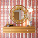 A floating shelf and statement mirror hang on a wall papered in a geometric stripe pattern in orange, blue, red and cream.