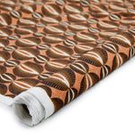 Partially unrolled fabric in an interlocking circular stripe print in shades of orange, brown and black on an orange field.