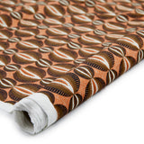 Partially unrolled fabric in an interlocking circular stripe print in shades of orange, brown and black on an orange field.