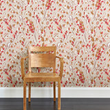 A wooden chair stands in front of a wall papered in a painterly leaf print in pink, brown and tan.