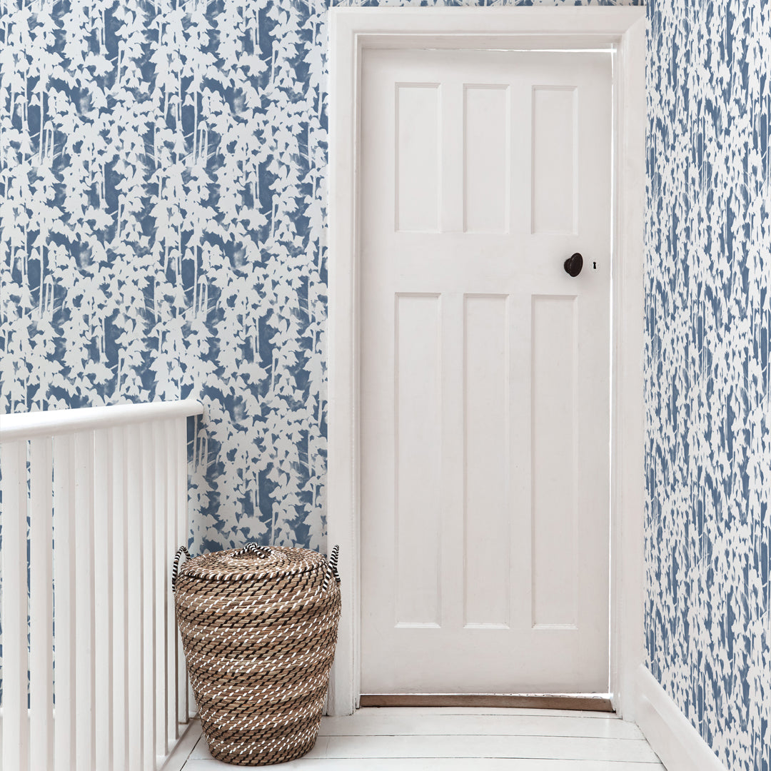 A door stands at the end of a hallway papered in a painterly bluebell pattern in white on a mottled blue field.