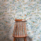 A wooden chair stands in front of a wall papered in a dappled abstract print in shades of blue, green, orange and white.