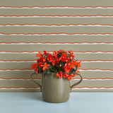 A vase of flowers stands in front of a wall papered in an undulating stripe pattern in coral, white and tan.