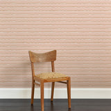 A wooden chair stands in front of a wall papered in an undulating stripe pattern in pink, white and rust.