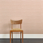 A wooden chair stands in front of a wall papered in an undulating stripe pattern in pink, white and gold.