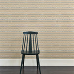 A wooden chair stands in front of a wall papered in an undulating stripe pattern in gray, white and tan.