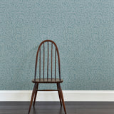 A wooden chair stands in front of a wall papered in a minimalist floral print in navy on a blue field.